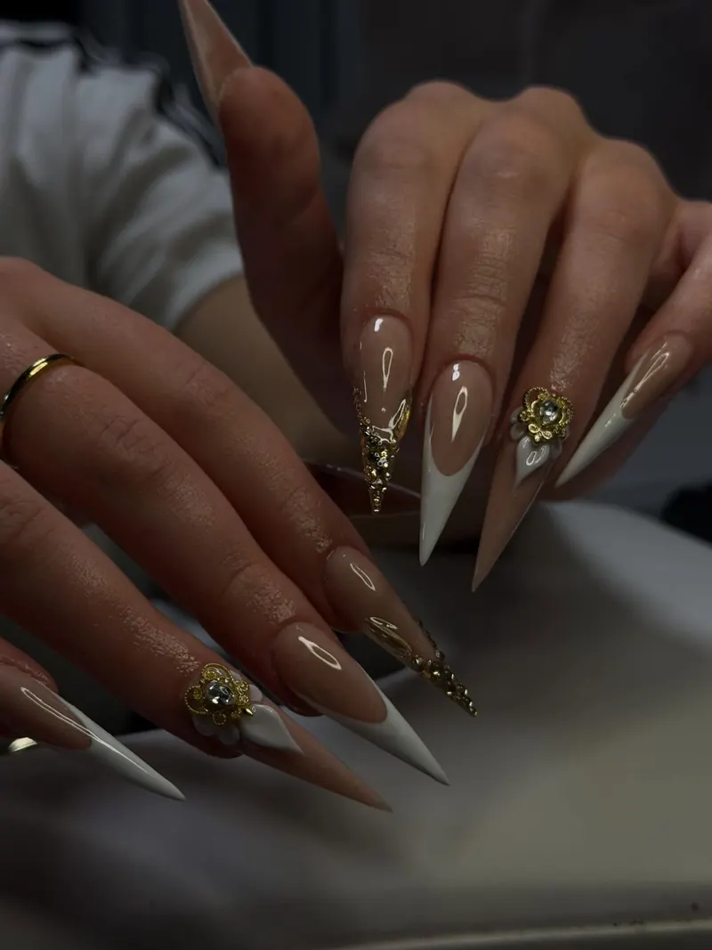 Long nude stiletto nails with white French tips and gold 3D charms