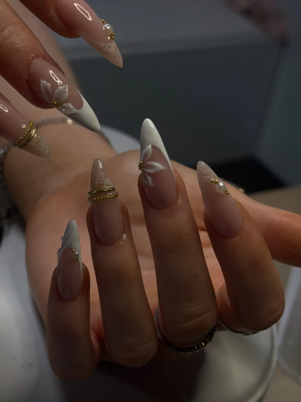 Nude almond nails with white lace flowers and gold rings